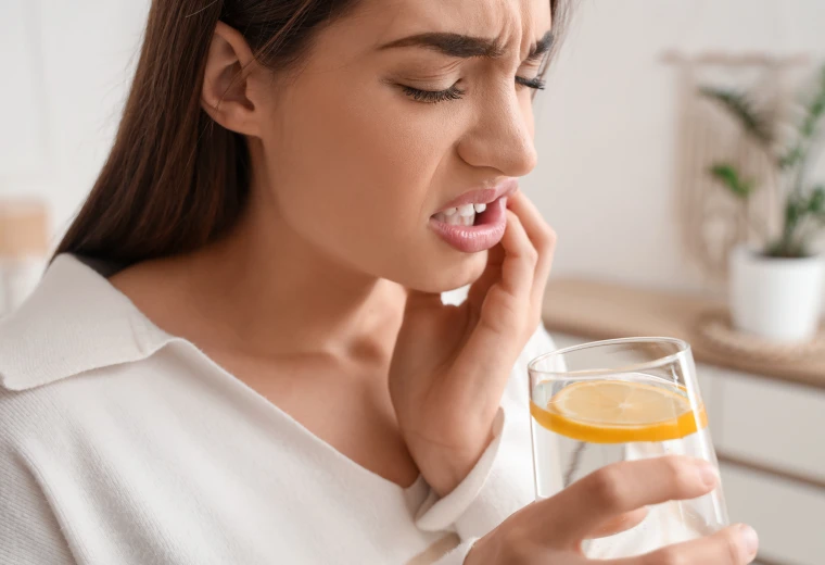 Femme ressentant une douleur dentaire et une sensibilité au froid en buvant un verre d'eau