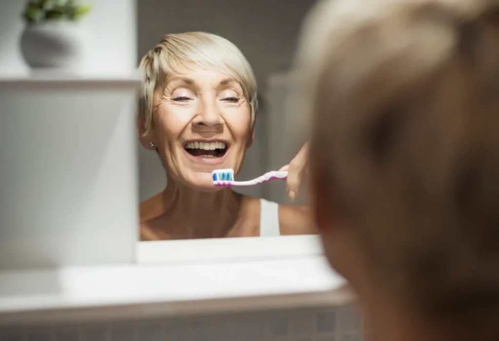 Patiente senior se brossant les dents devant un miroir après pose d'une prothèse sur implants